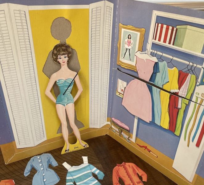 A paperboard folder stands open with a paper doll standing/leaning against it. On the lefthand side of the folder, a dressing room is represented by white louvered doors shown in an open position. From the yellow rectangle between them, the doll has been punched out. The paper doll has brownette bubble cut hair and wears a strapless one-piece undergarment with black open-toed shoes. The righthand side of the folder shows a closet filled with dresses and hatboxes on the shelf above. Differently colored belts hang on the open door. To the left of the closer is a framed picture of a ballerina, and below that, a notepad. A low, pink-cushioned stool sits beneath them next to the closet, and two pairs of closed-toed shoes in red and pale blue sit near the stool.
