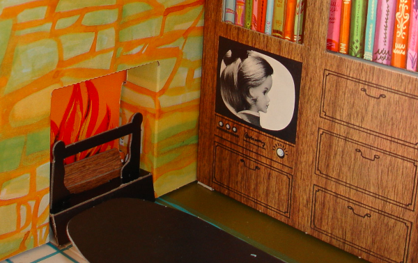 Close up on wood-look chipboard shelves, with drawn-on drawers and colorful book spines, next to fireplace with orange and green fieldstone. Black-and-white TV is illustrated into the shelving and shows Tressy in profile, her hair grown out, wearing what looks like her original red-and-white dress (but only hear and shoulders are shown).