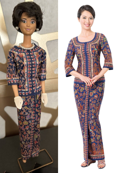 Doll and human wear long wrap skirt and matching top with mid-length sleeves. Garments are in deep blue with red and gold floral and nonrepresentational designs. Human wears strappy cris-cross sandals in the same colors as the sarong kebaya. Doll is barefoot but originally wore plastic navy strappy-look sandals.